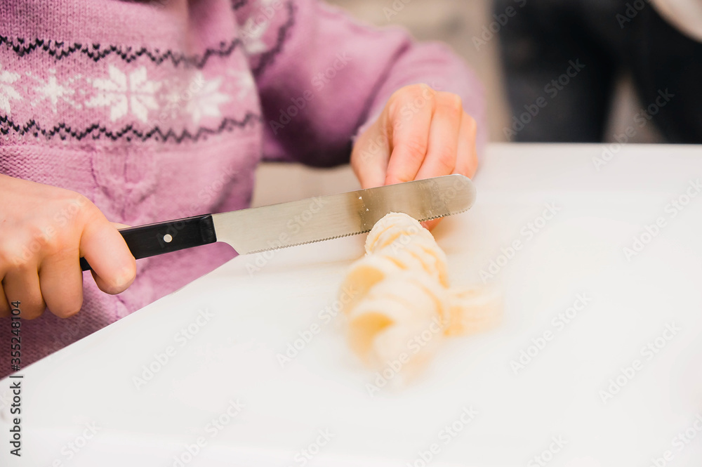 The child cooks. The girl's hands crumble a banana for fruit salad with a knife. Kids' cooking class on baking The child cooks. The girl's hands crumble a banana for fruit salad with a knife. Kids' cooking class on baking