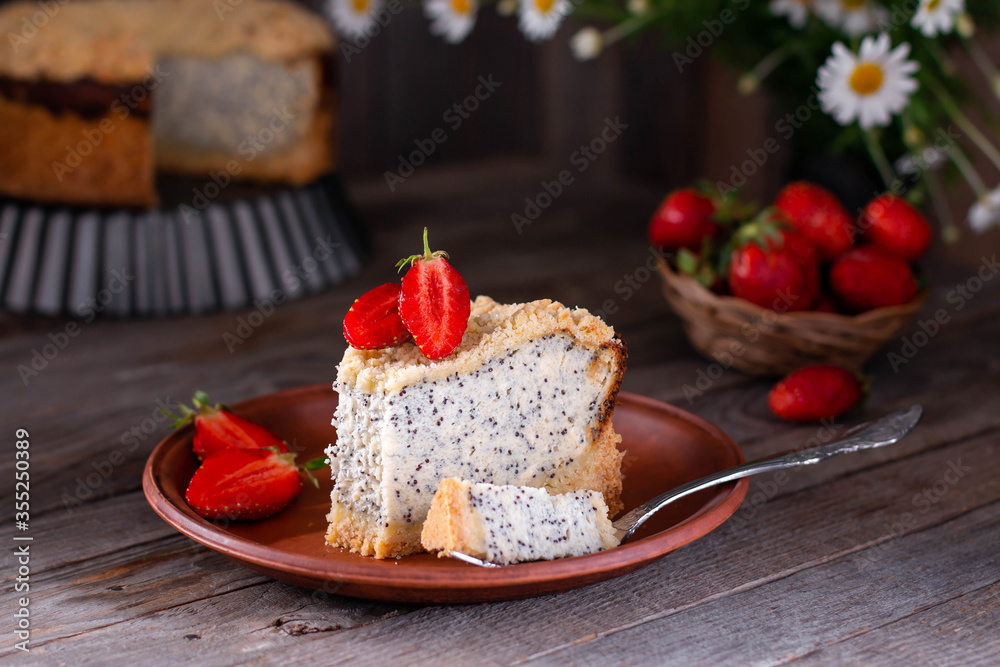 Homemade poppy seed cheese cake in a ceramic plate on an wooden background with flowers and strawberries on a background