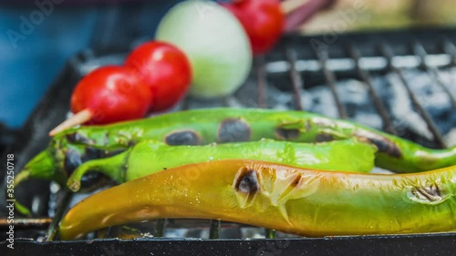 Cinemagraph of smoke emitted from cooking tomato, onion, and green chili pepper on a hot BBQ grill. Close up, loop with selective focus.