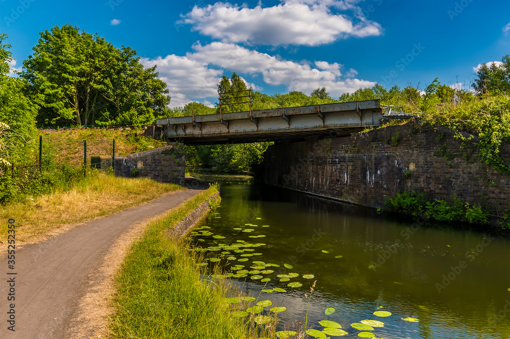 Fototapeta premium A view towards a railway bridge over the Birmingham Canal in summertime