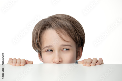  boy peeping from behind a white table, the portrait of boy looks out, a sly look, free copy space,