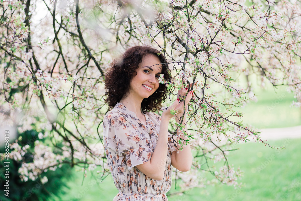 Young attractive woman with curly long hair posing in spring blooming garden, apple trees Young attractive woman with curly long hair posing in spring blooming garden, apple trees