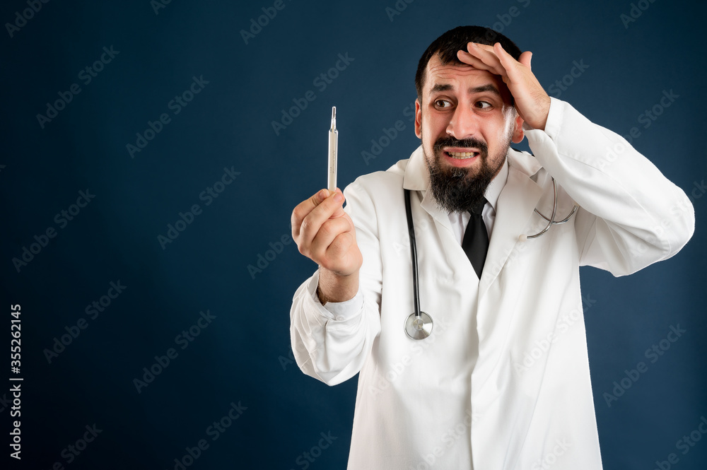 Male doctor with stethoscope in medical uniform is looking at the thermometer Male doctor with stethoscope in medical uniform is looking at the thermometer