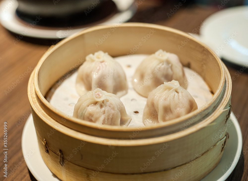 Kuala Lumpur, Malaysia - January 21, 2020 :Closeup 4 pieces of Streamed Pork Dumpings of Shanghai Xiao Long Bao serve in traditional round bamboo basket. Kuala Lumpur, Malaysia - January 21, 2020 :Closeup 4 pieces of Streamed Pork Dumpings of Shanghai Xiao Long Bao serve in traditional round bamboo basket.