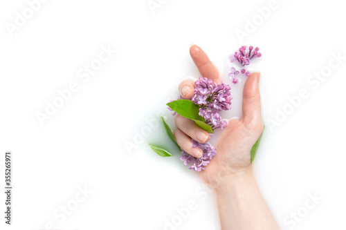 Girl's palm of a girl in a bath with milk and flowers. Copy space, flat lay. The concept of purity, tenderness, freshness, youth. Lilac flowers.