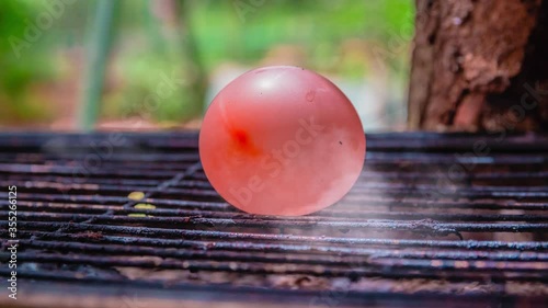 Cinemagraph of smoke emitted from a hot BBQ grill with a water balloon placed on it. Close up, loop with selective focus.