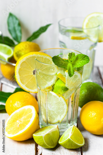 Concept of summer refreshing healthy alcohol free homemade lemonade with fresh pepper mint, limes and lemons. Low calories cold detox beverage. Wooden background, closeup
