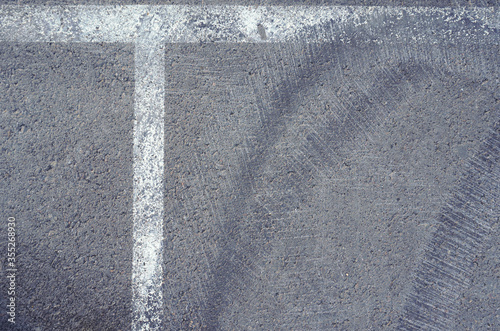 Asphalt texture with white line and tire marks.  Smooth asphalt road. Tarmac dark grey grainy road background.Top view