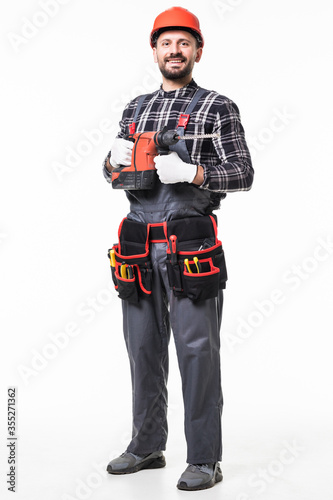 Handsome handyman in uniform with tool belt holding drill isolated on white