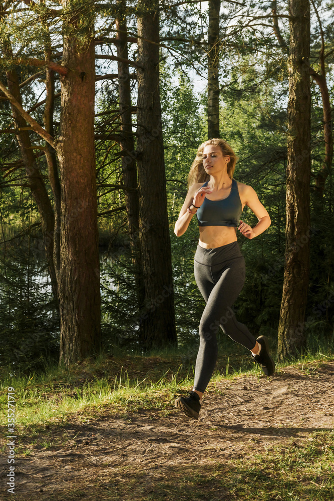 Young slim athletic woman getting ready for a marathon while running through the forest Young slim athletic woman getting ready for a marathon while running through the forest
