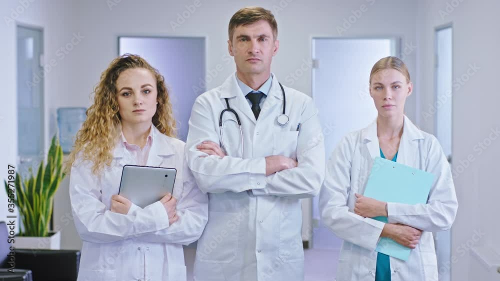 Mature man doctor and his nurse assistance standing in front of the camera in the middle of the hospital corridor and holding digital tablet and map Mature man doctor and his nurse assistance standing in front of the camera in the middle of the hospital corridor and holding digital tablet and map