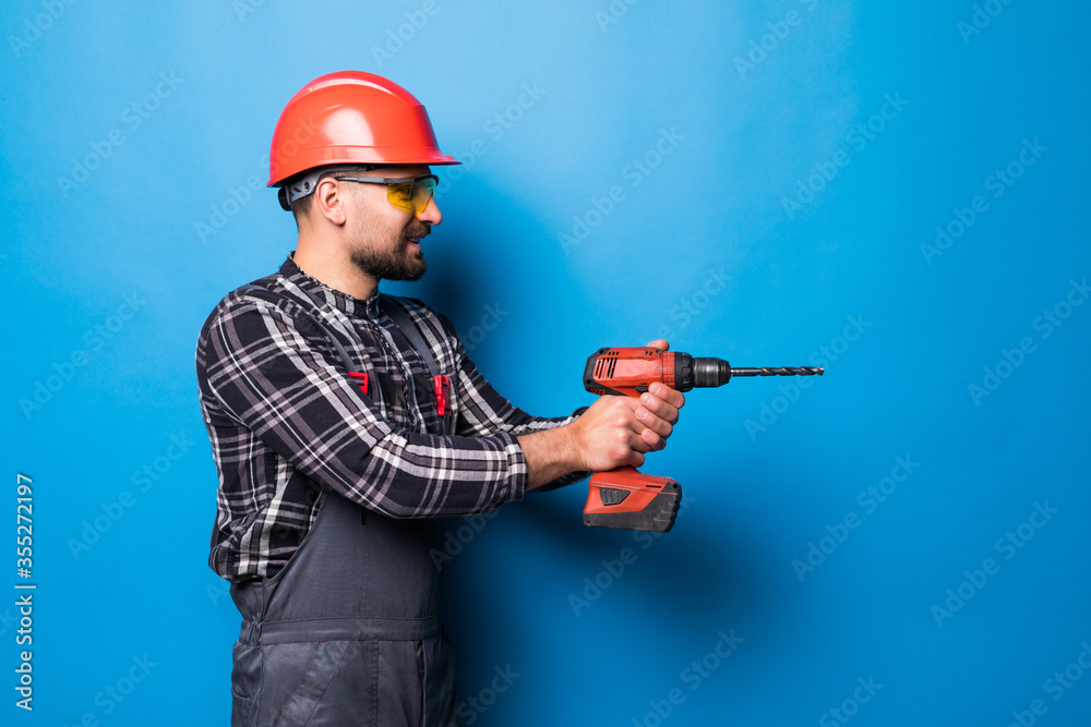 Young repairman with drill perforator isolated on blue background Young repairman with drill perforator isolated on blue background