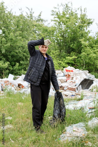 a middle-aged man in black clothes puts grbage in a black bag photo