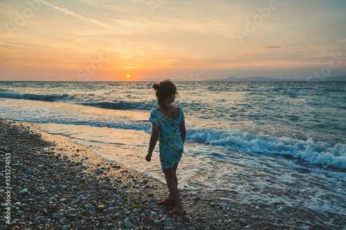 Small girl on pebble beach during sunset. West coast of Island of Rhodes. Greece.