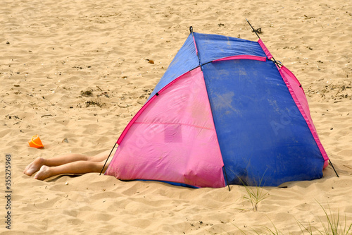 Pair of legs protruding from a tent on a sandy beach  © Cerib