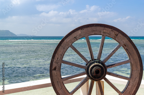 close-up of an old wooden steering wheel in tropical seascape. sky and sea are blue with some clouds
