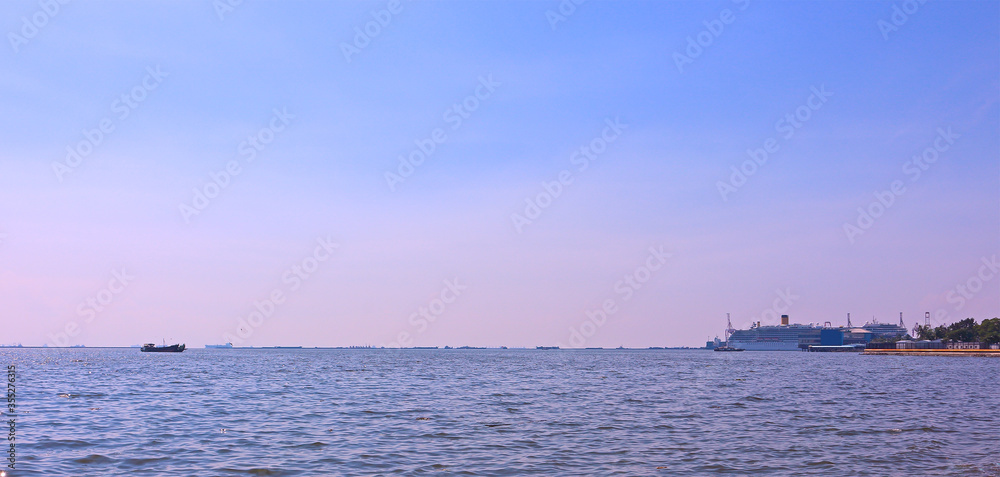 Beautiful sunset colors and sea view with an ocean liner on the horizon in the seaport. Seascape for travel, advertising and holidays backgrounds