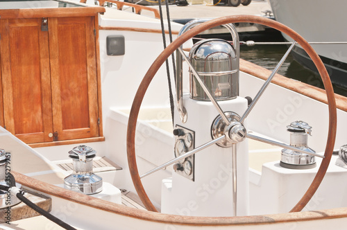 Front view, close distance of a pilot station of a luxury sailboat, with sterring wheel, compass, wood door and automatic cleats © reve15