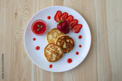 Three pancakes with cheese and strawberries and sauce on a white dish against wood background. Delicious cheese pancake and strawberries for the breakfast or lunch. Tasty meal with berries.