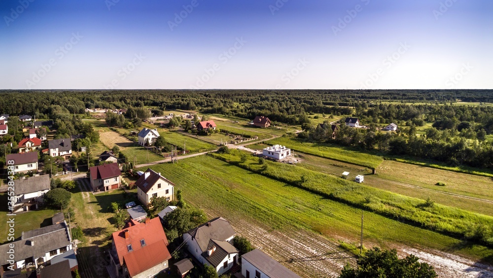 Aerial view on small village in central Poland surrounded by forest. Several houses and empty building plots to be developed.  House under construction in center.