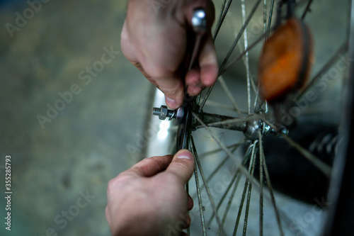 Bicycle repair. Old rusty wheel. The mechanic in the workshop, in his hand holds a wrench. On the spokes hanging cobwebs and dust. Top view of the wheel hub. Tool and hands of a repairman close up.