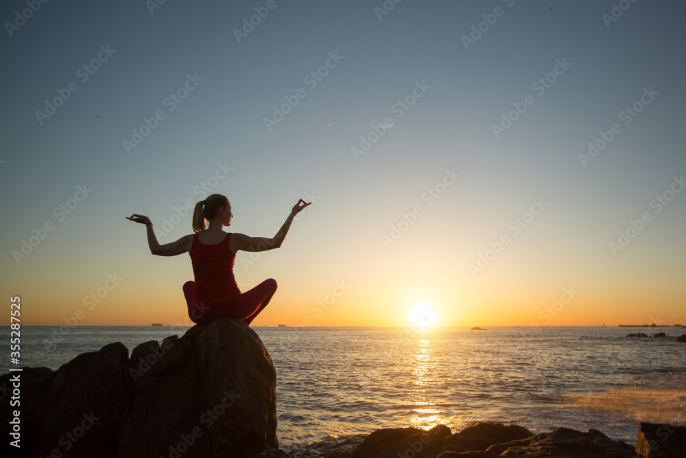 Silhouette of yoga woman at meditation on the sea beach during sunset.