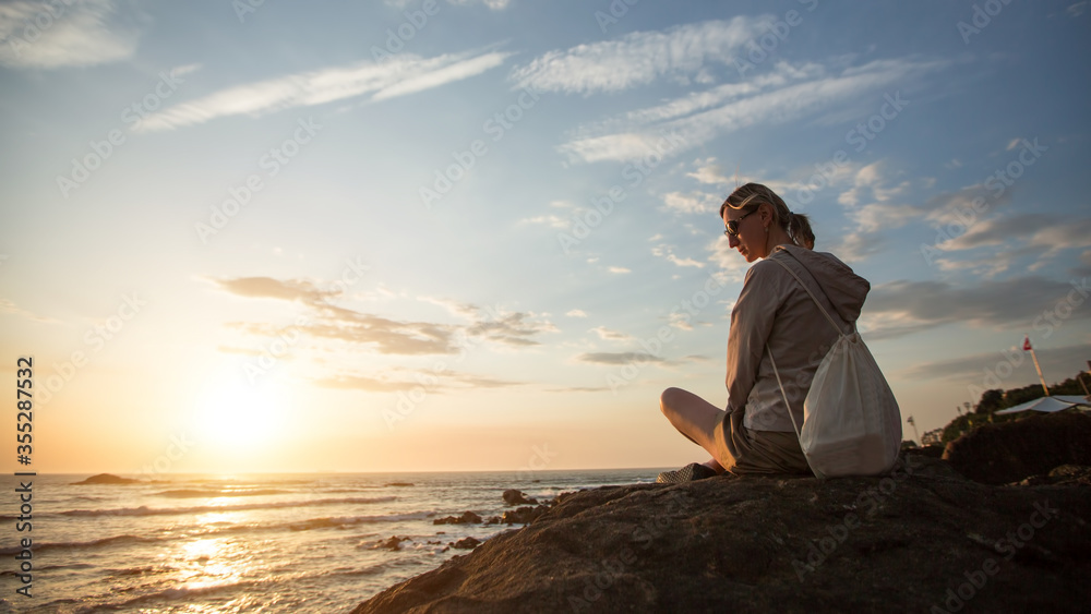 Fototapeta premium A young woman sitting on the rocky Atlantic coast during sunset