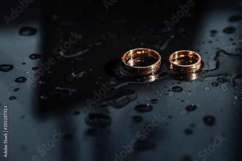 Wedding rings on a black glass with water. Wedding concept. Wedding minimalism. Gold wedding rings.