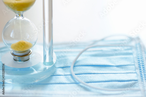 Hourglass on the background of a blue mask to protect against the virus. Concept of the course and end of the quarantine of the disease and pandemic of the coronavirus COVID-19