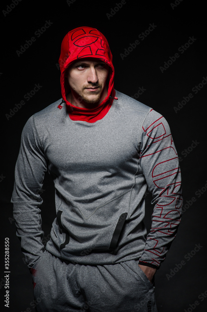 A sporty guy stands in the Studio against a dark background in a hood. Sports, beauty A sporty guy stands in the Studio against a dark background in a hood. Sports, beauty