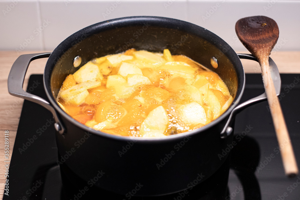 Homemade apricot jam, boling in a black pot with a wooden spoon on the side. Preparing seasonal fruit preserve on induction stove. Homemade apricot jam, boling in a black pot with a wooden spoon on the side. Preparing seasonal fruit preserve on induction stove.