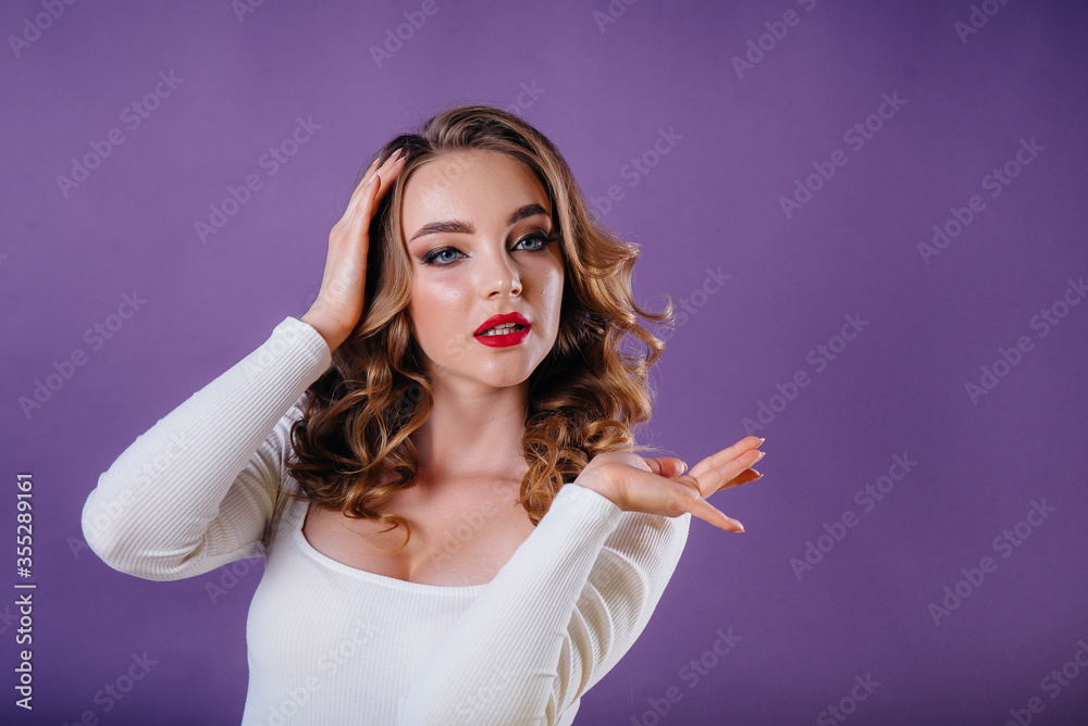 Obraz premium A young beautiful girl shows emotions and smiles in the Studio on a purple background. Girls for advertising