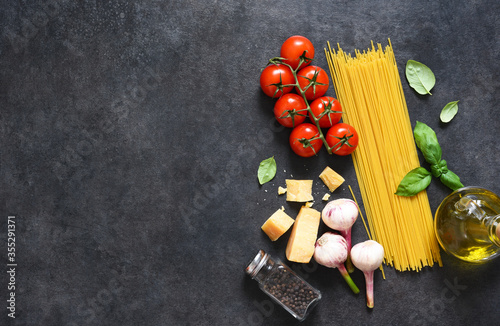Ingredients for making pasta. Raw spaghetti with tomato and basil on a black background. View from above.
