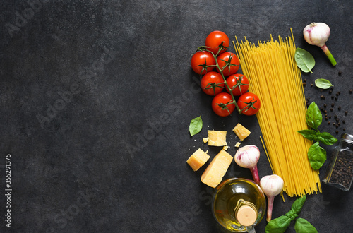 Ingredients for making pasta. Raw spaghetti with tomato and basil on a black background. View from above.