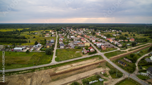 Aerial view on small village located in central Poland. Summer landscape, cloudy afternoon. Green meadows, calm light. Small detached houses, streets, railroad.