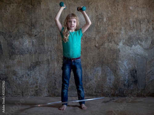 girl teenager in green T-shirt and jeans does gymnastics with dumbbells in  studio. child twists gymnastic ring