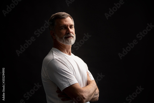 Portrait of smiling mature man standing on black background. © opolja