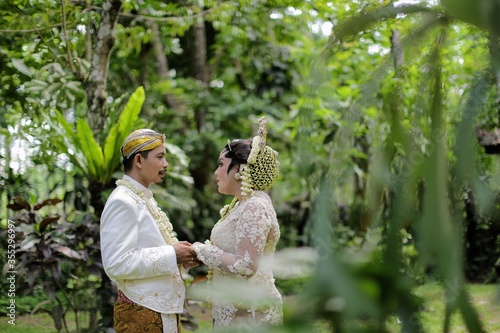 Wedding shot of bride and groom stand in park. With indonesian traditional costume. Java white bridal concept.