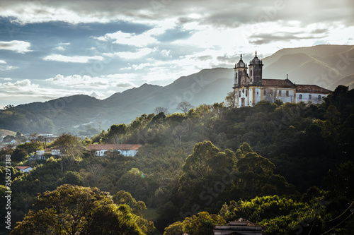 Landscape of Ouro Preto city of Minas Gerais, Brazil with Sao Francisco de Paula Church at foreground with sunlight and clouds rounded by green florest and trees  photo