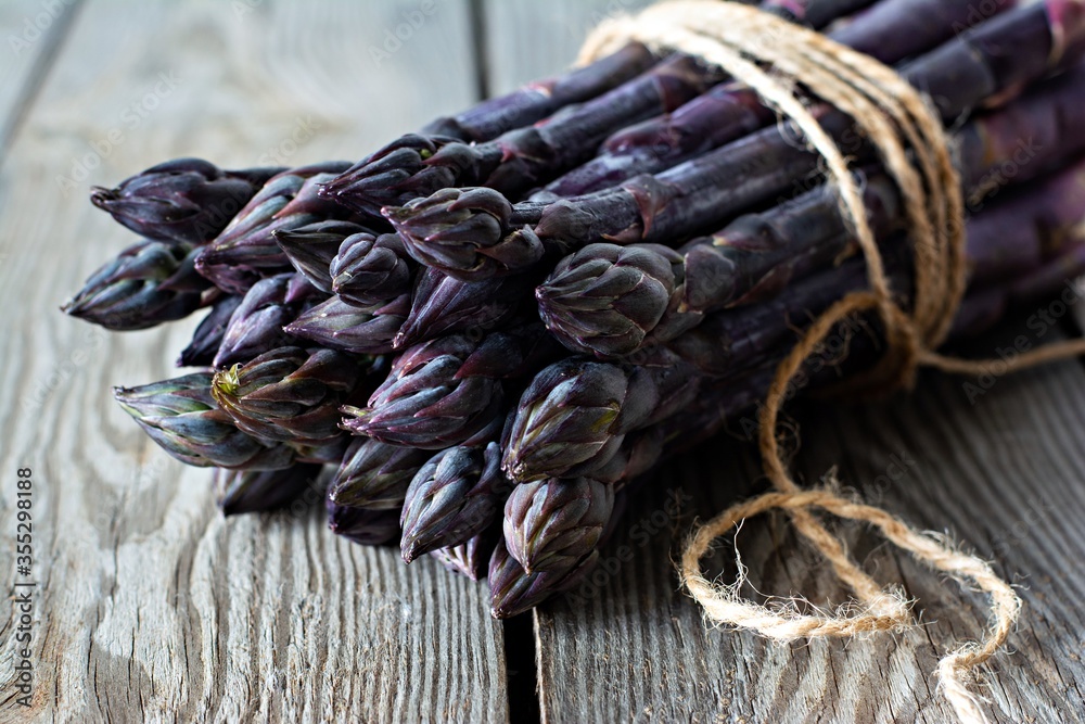 Fresh bunch of purple asparagus on a wooden background.