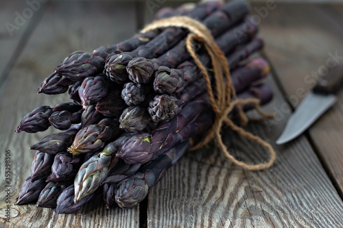 Fresh bunch of purple asparagus on a wooden background.