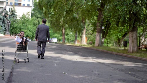 Wallpaper Mural Businessman pulls boss woman in a shopping cart who talking on a shoe like on the phone outdoors and leave her and walk away. Boss makes employees to entertain her. Harassment at work. Prores 422. Torontodigital.ca