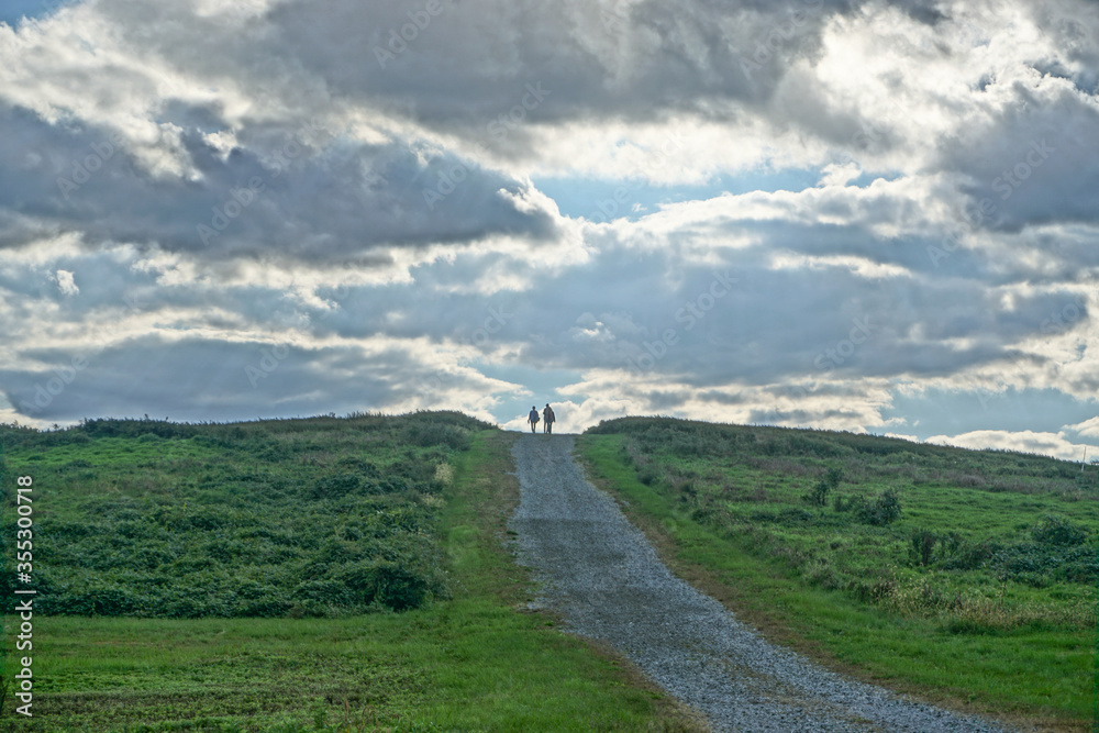 Croton-On-Hudson, New York, USA: Two people on a path, silhouetted under a cloud-filled sky, in Croton Point Park.