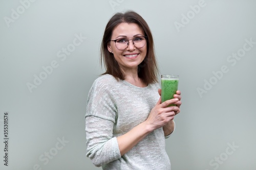 Mature woman with green vegetable smoothie drink, healthy vegan diet
