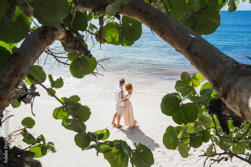 Newlyweds holding hands hugging at white sandy tropical caribbean beach landscape after wedding ceremony of marriage on destination wedding honeymoon travel looking on blue sea in Punta Cana Dominican