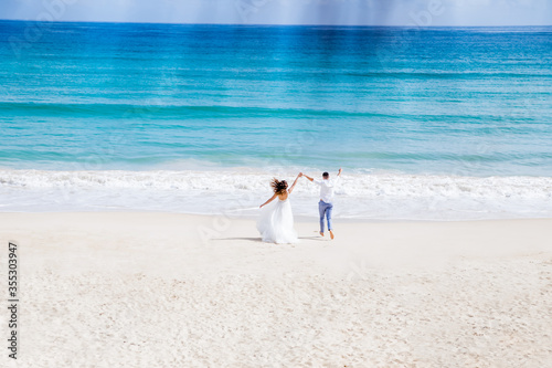 Fototapeta Newlyweds holding hands hugging at white sandy tropical caribbean beach landscap