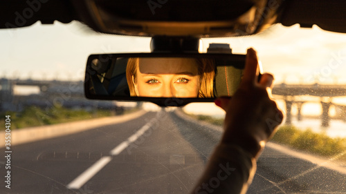 Tableau sur toile Cheerful joyful woman adjusting mirror while sitting in her car, looking in reflection at camera