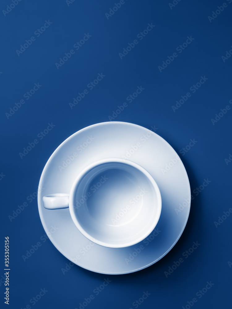 Flat lay. Empty white cup on a saucer on a blue background. Trend color. Classic blue. Copy space. Flat lay. Empty white cup on a saucer on a blue background. Trend color. Classic blue. Copy space.