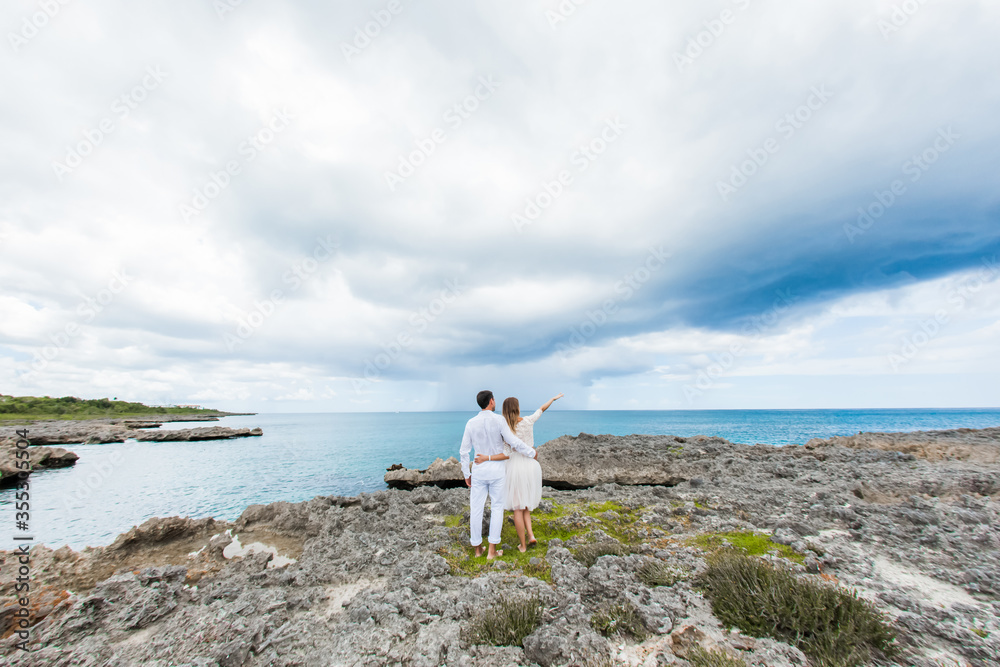 Newlyweds holding hands hugging at white sandy tropical caribbean beach landscape after wedding ceremony of marriage on destination wedding honeymoon travel looking on blue sea in Punta Cana Dominican