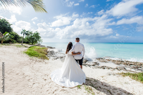 Obraz na płótnie Newlyweds holding hands hugging at white sandy tropical caribbean beach landscap